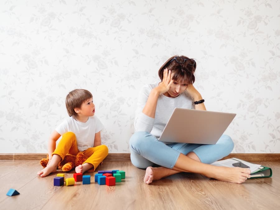 mom stressed on computer with child nearby