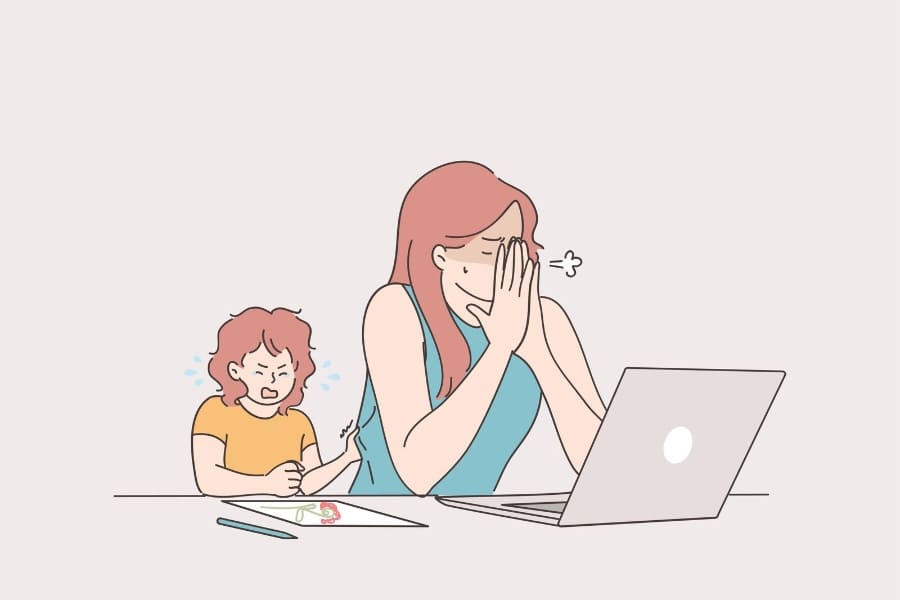 mom struggling with work on computer while child draws close by